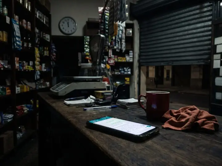 Celular con WhatsApp abierto sobre el mostrador de un almacén cerrado, de noche